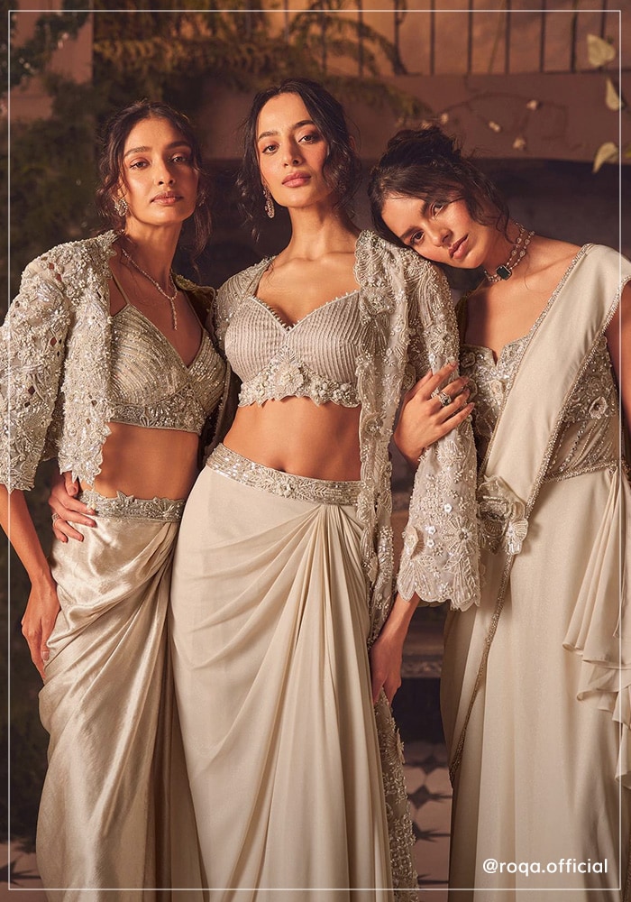 Three models wearing Roqa outfits. Two wearing a jacket and skirt set and one wearing a pre-draped saree