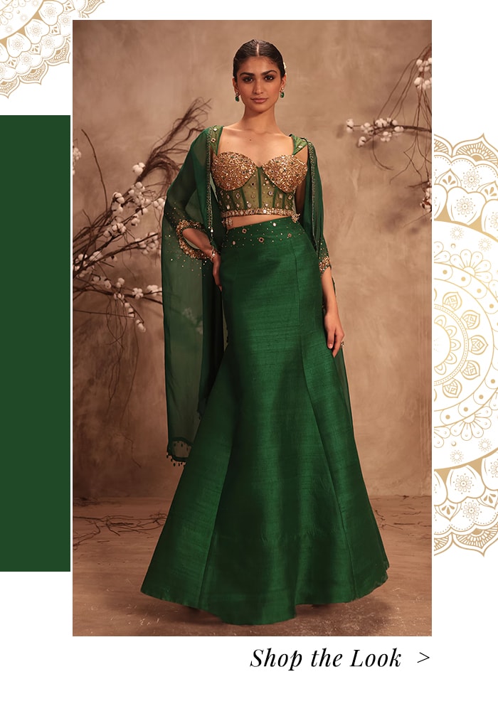 Model wearing green cape paired with a monotone lehenga skirt and embroidered corset blouse