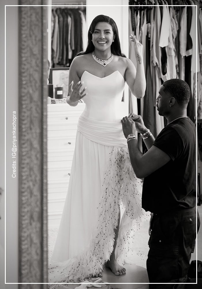 Priyanka Chopra Jonas in strapless white Dior gown with ostrich 
feather trim posing against wall in black and white editorial 
shot before Oscars 2026