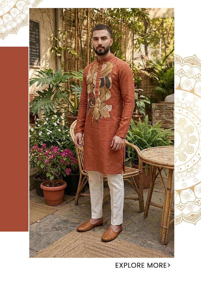 Terracotta linen kurta for men with large floral kalamkari embroidery on the placket, styled with cream trousers and tan juttis at a green outdoor café — Aza Fashions