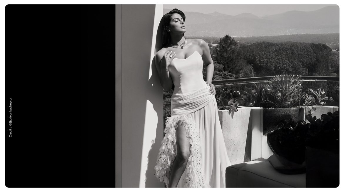Priyanka Chopra Jonas in custom white Dior gown with feather hemline and thigh high slit posing on outdoor terrace before Oscars 2026
