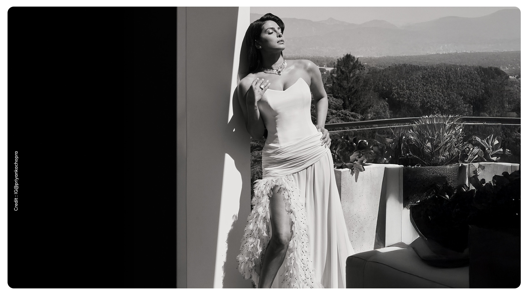 Priyanka Chopra Jonas in custom white Dior gown with feather hemline and thigh high slit posing on outdoor terrace before Oscars 2026