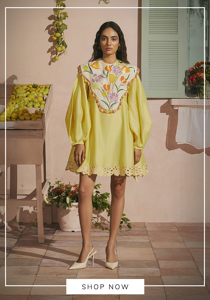 Woman wearing a pastel yellow embroidered mini dress with statement floral yoke and balloon sleeves paired with white heels