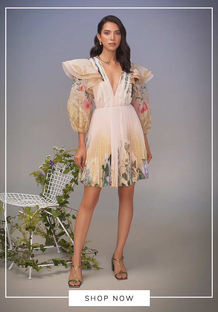 Woman wearing a blush floral pleated mini dress with dramatic ruffle shoulders and puff sleeves, styled for an elegant Mahjong party